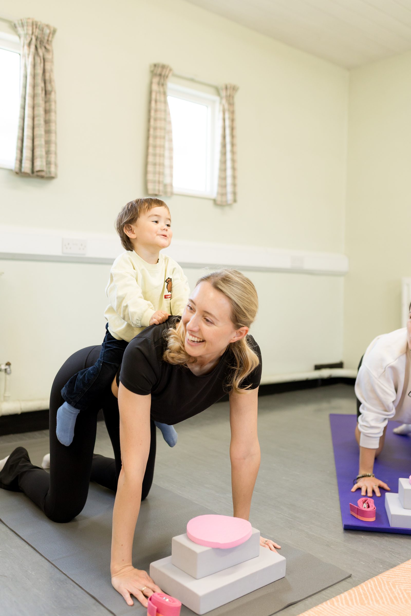 Amber holding a plank with a smiling toddler balanced on her back during Flow Mama class